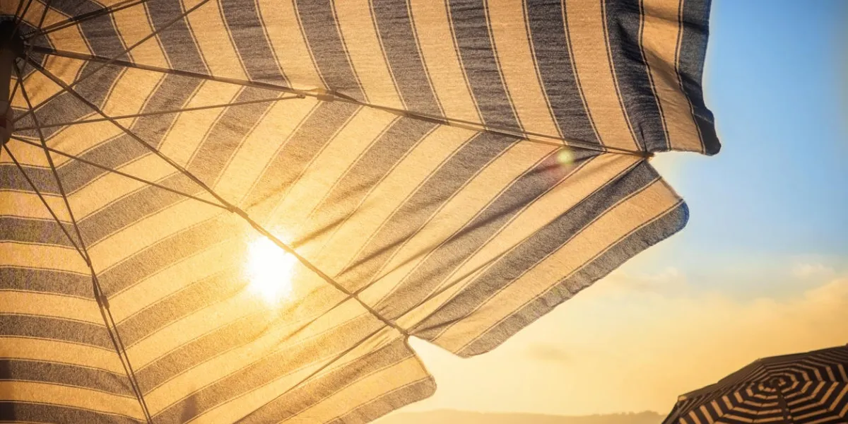umbrella and sun in front at sunset on sandy city beach on sea shore ocean concept of tourism travel and body skin protection from melanoma skin cancer sunburn umbrella and sun in front at sunset on sandy city beach on sea shore ocean concept of tourism travel and body skin protection from melanoma skin cancer sunburn