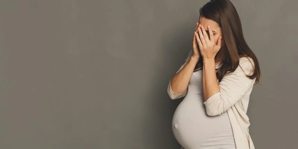crying pregnant woman portrait, gray studio background, copy space depressed expectant lady close her face pregnancy emotions and hormones concept