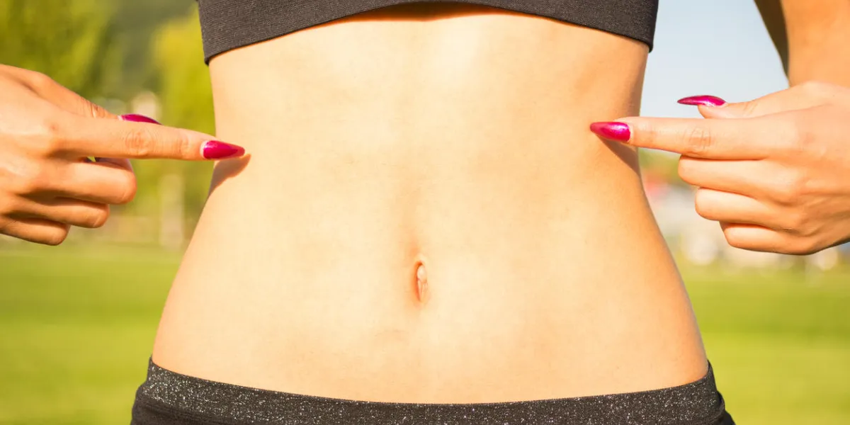 closeup of woman pointing finger at her well trained tummy outdoors