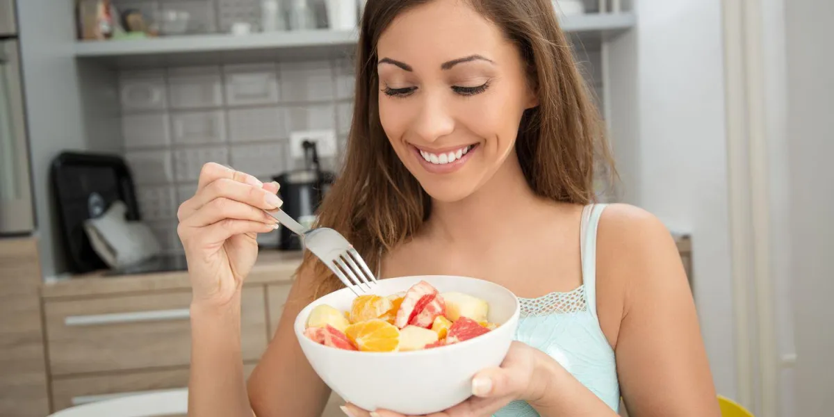 belle jeune femme souriante, manger une salade de fruits dans la cuisine