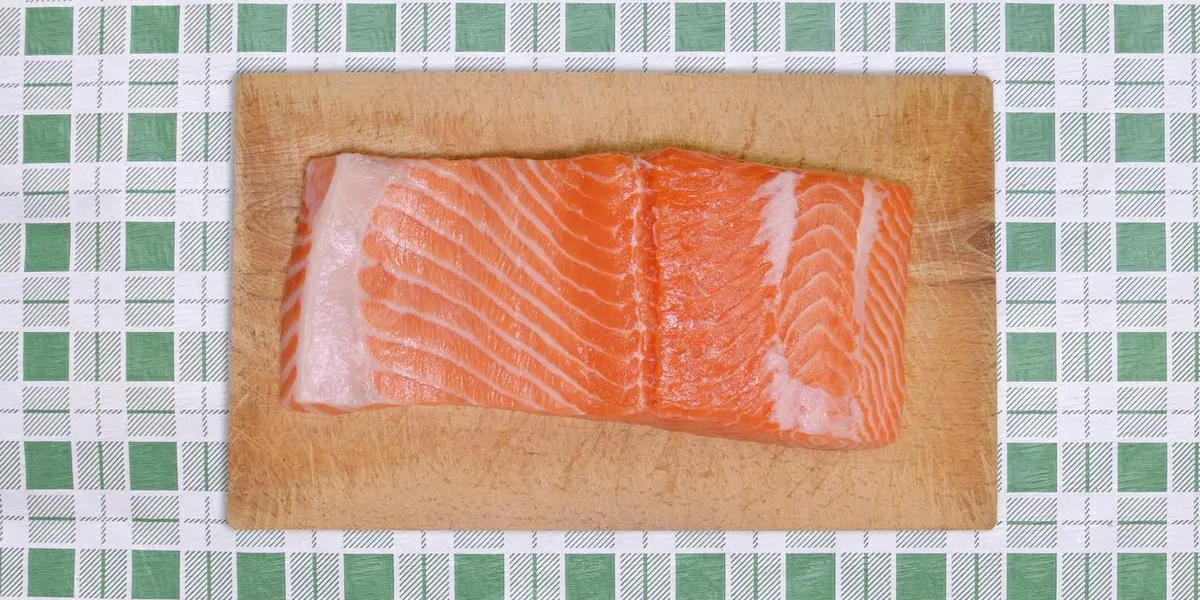 fresh salmon fish on wood cutting board green plaid tablecloth