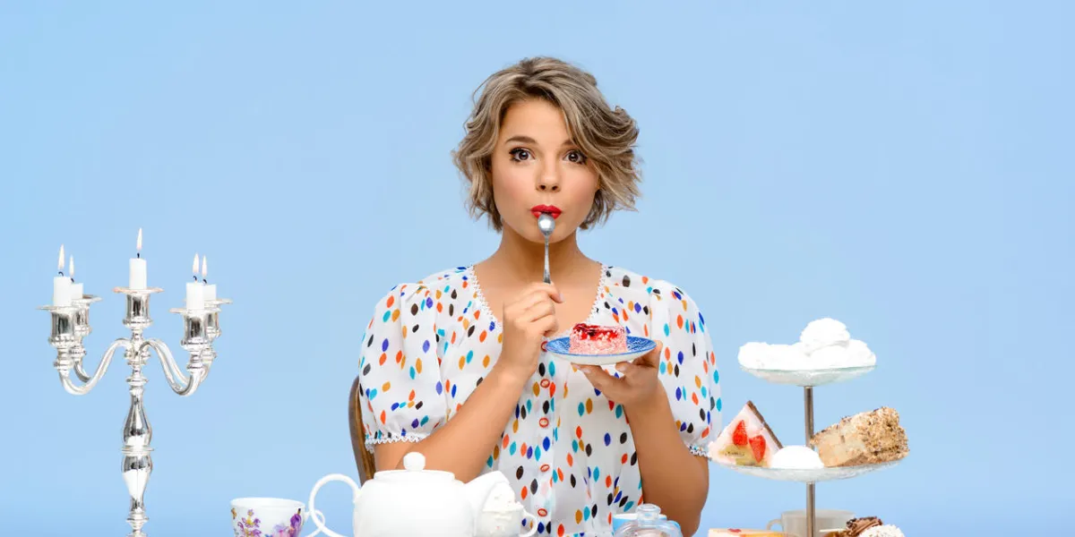 portrait de jeune fille belle en blouse blanche, assis à table avec des bonbons, en regardant la caméra, manger des desserts sur fond bleu portrait de jeune fille belle en blouse blanche, assis à table avec des bonbons, en regardant la caméra, manger des desserts sur fond bleu
