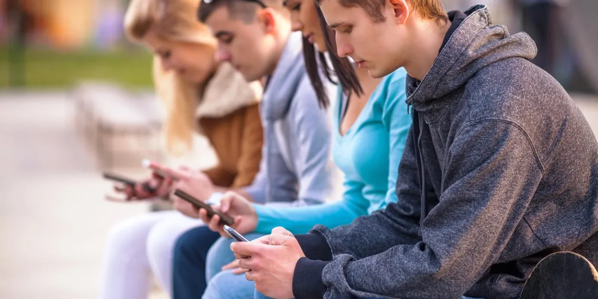 group of teenagers sitting outdoors using their mobile phones