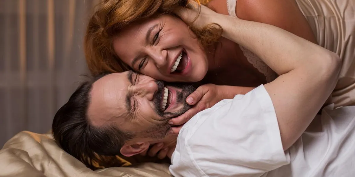 portrait of excited married couple lying on bed and laughing they are hugging with closed eyes