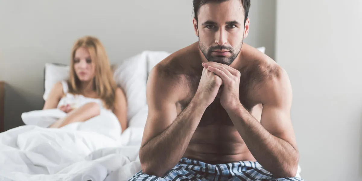 abused young man is sitting on bedside and looking at camera with sadness his wife is lying and expressing frustration on background portrait abused young man is sitting on bedside and looking at camera with sadness his wife is lying and expressing frustration on background portrait