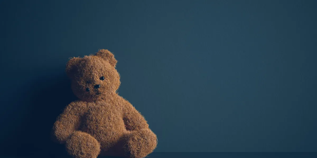 teddy bear with torn eye sits in dark room child abuse and violence concept