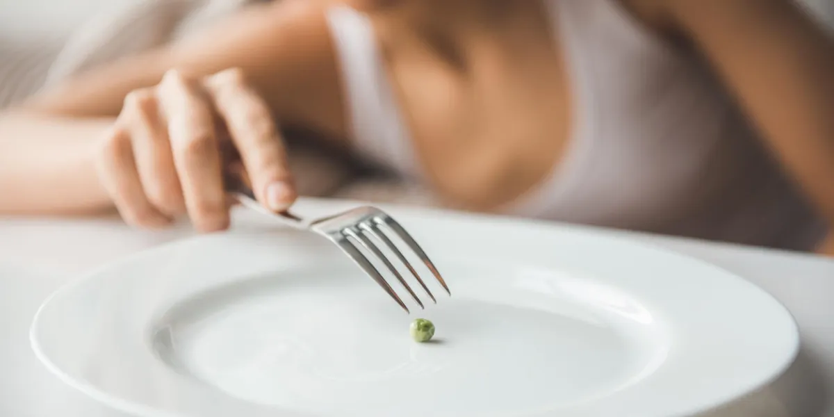 suffering from anorexia cropped image of girl trying to put a pea on the fork