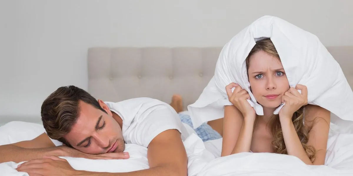femme en colère tenant oreiller à côté d'un homme endormi dans son lit femme en colère tenant oreiller à côté d'un homme endormi dans son lit