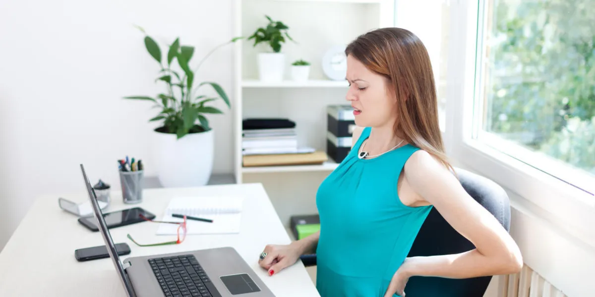 image d'une jeune femme ayant mal au dos alors qu'elle était assise au bureau de travail