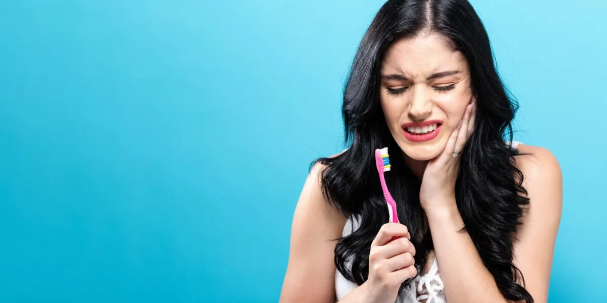 young woman holding a toothbrush on a solid background