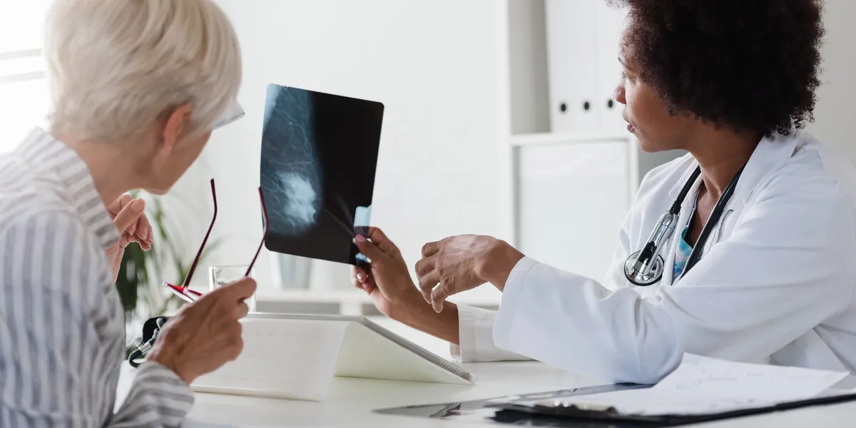 a female doctor sits at her desk and talks to a female patient while looking at her mammogram brest cancer prevention