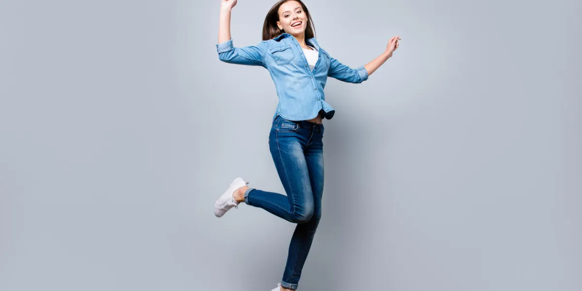 happiness, freedom, power, motion and people concept - full length portrait of smiling young woman jumping with raised fists over grey background