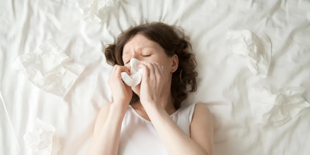 young depressed or sick with flu model lying on the bed with closed eyes and blowing her nose into tissue view from above young depressed or sick with flu model lying on the bed with closed eyes and blowing her nose into tissue view from above
