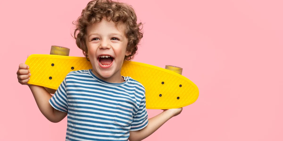 charming curly boy holding yellow longboard and looking away on pink background charming curly boy holding yellow longboard and looking away on pink background
