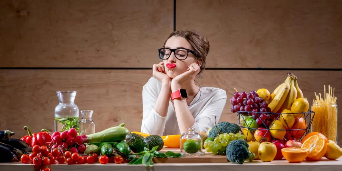young and sad woman thinking about tasty food and calories sitting at the table full of fruits and vegetables in the wooden interior