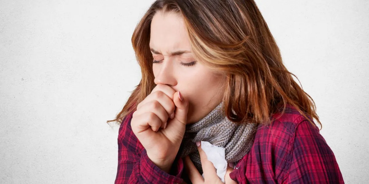 studio shot of beautiful young female model has bad cough, uses tissue, wears scarf on neck, feels unwell and unhealthy, isolated over white concrete background sickness and illness concept