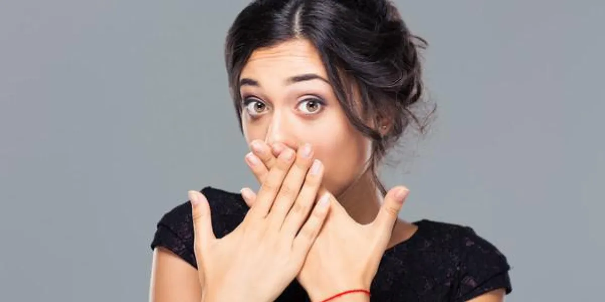 portrait d'une jeune femme couvrant sa bouche sur fond gris et regardant la caméra