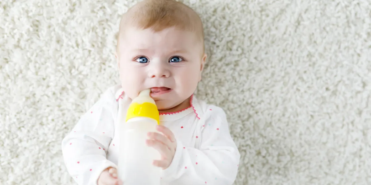cute adorable newborn baby girl holding nursing bottle and drinking formula milk first food for babies new born child, little girl laying on white background family, new life, childhood, bottle-feeding concept