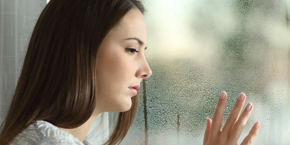 sad woman looking the rain falling through a window at home or hotel