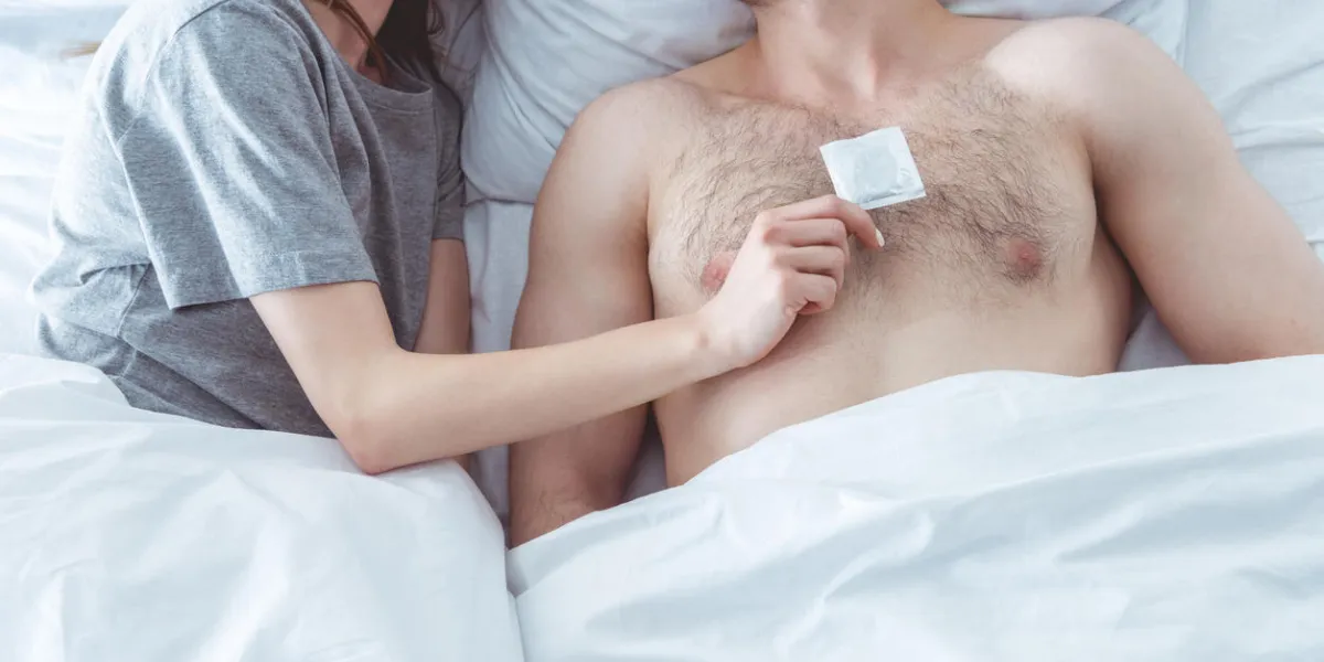 cropped view of couple with condom lying in bed cropped view of couple with condom lying in bed
