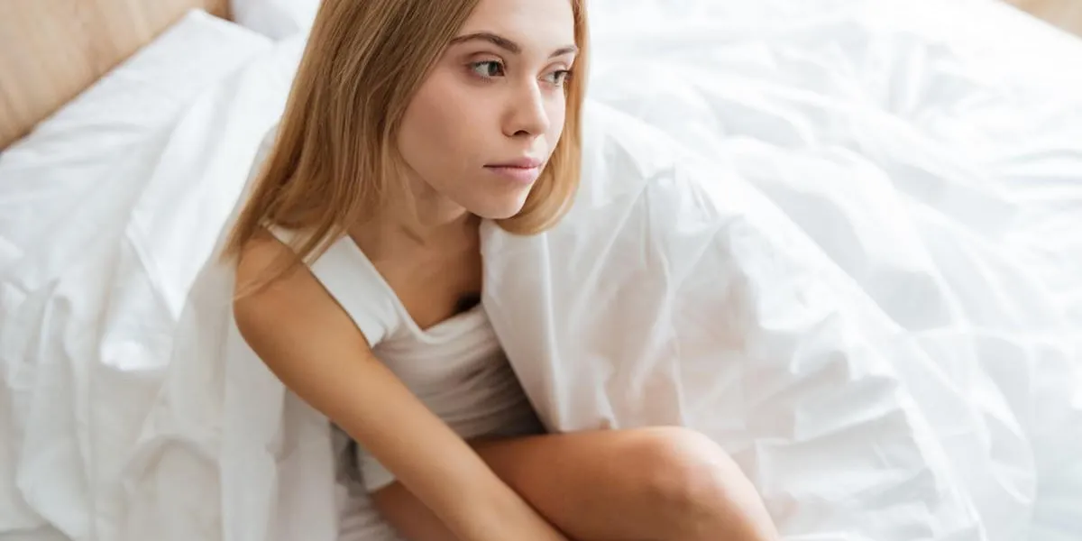 vue de dessus de gentil jeune femme réfléchie, assis et penser au lit à la maison