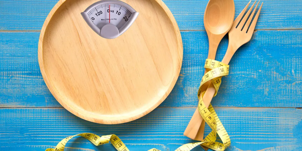 scale shaped on the wood plate with a fork and spoon, blue background diet and healthy concept scale shaped on the wood plate with a fork and spoon, blue background diet and healthy concept
