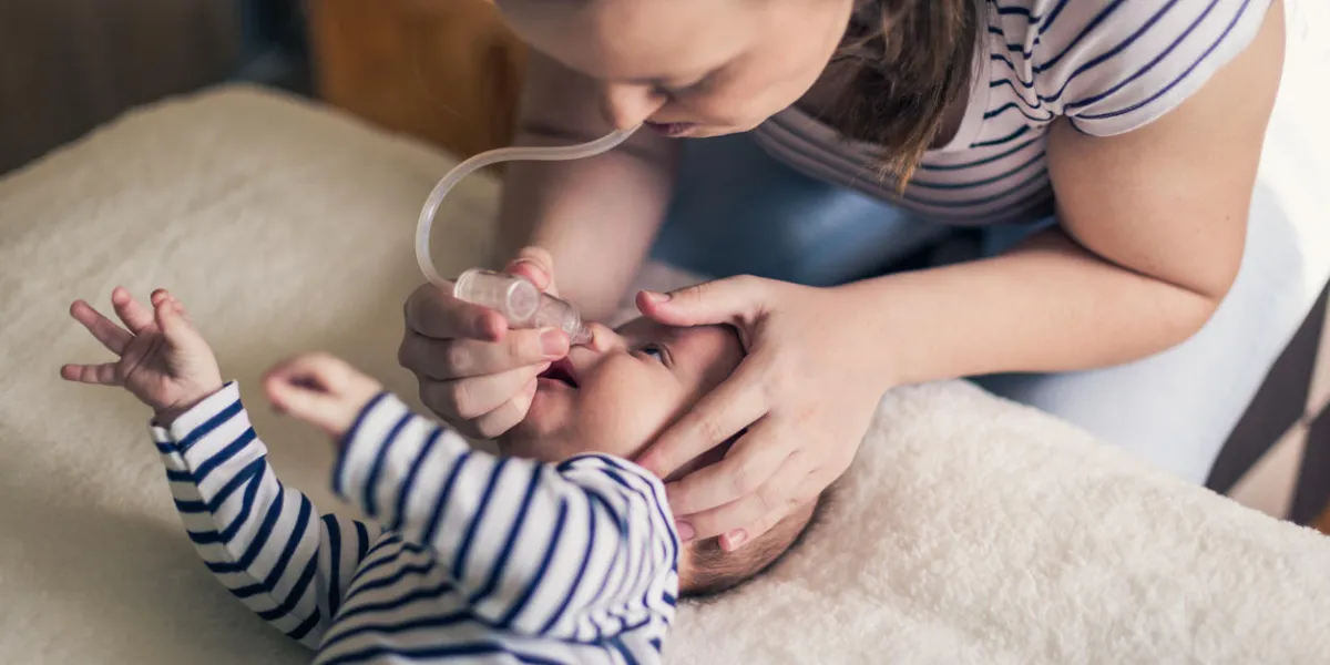 young single mother cleans a nose of a two months old baby boy on the bed using the nose aspirator they are dressed in matching white and blue striped clothes young single mother cleans a nose of a two months old baby boy on the bed using the nose aspirator they are dressed in matching white and blue striped clothes