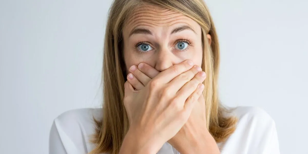 close-up of face of frightened young caucasian woman wearing white shirt looking at camera and covering mouth speak no evil concept close-up of face of frightened young caucasian woman wearing white shirt looking at camera and covering mouth speak no evil concept