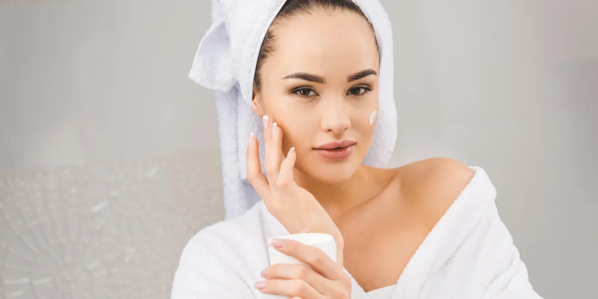 portrait of beautiful woman with towel on head holding face cream