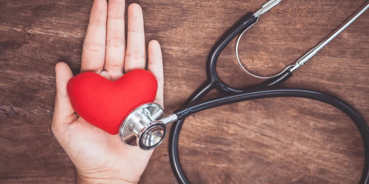 red heart on woman's hand with doctor's stethoscope on wooden background healthcare medical concept
