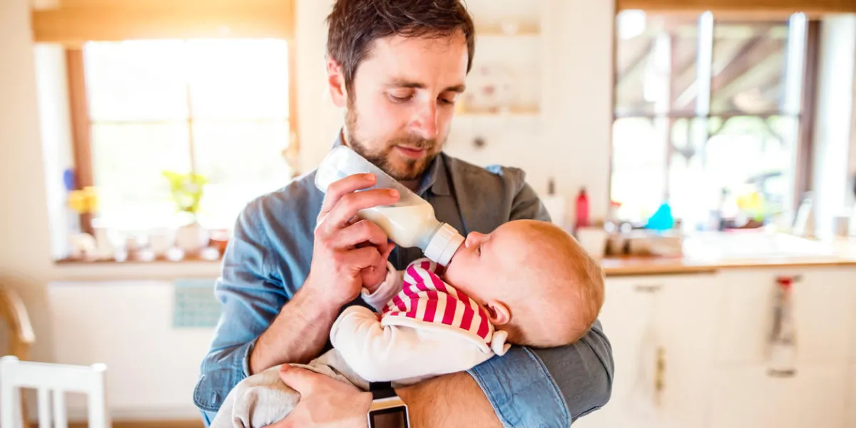 young father feeding his cute newborn baby son, holding him in his arms