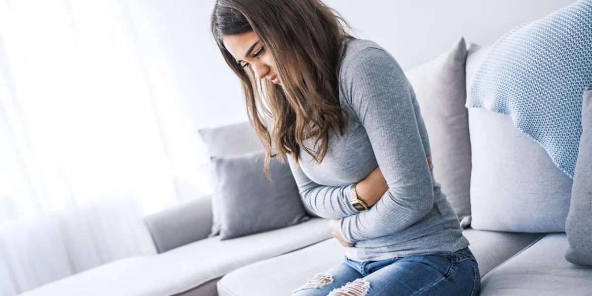 young woman suffering from abdominal pain while sitting on bed at home woman stomach pain young woman suffering from stomach ache while lying on sofa at home