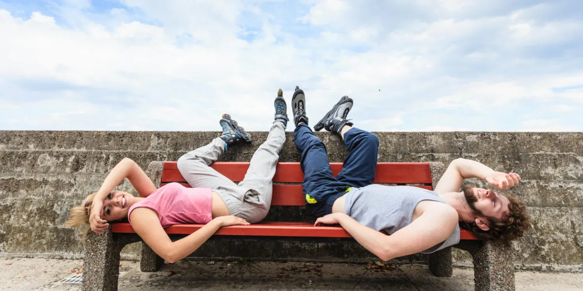 young tired people friends in training suit with roller skates woman and man relaxing lying on bench outdoor young tired people friends in training suit with roller skates woman and man relaxing lying on bench outdoor