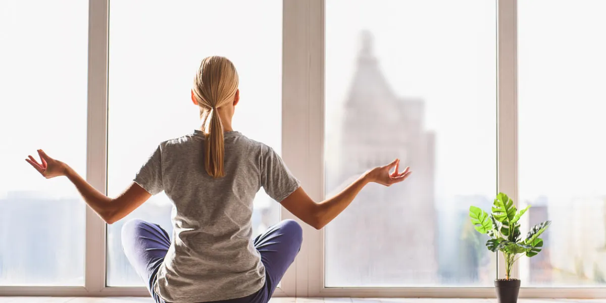 meeting new morning relaxed young woman is doing yoga at home she is sitting in lotus position in front of the window focus on her back