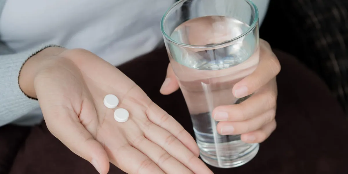 woman hand with pills medicine tablets and glass of water for headache treatment healthcare, medical supplements concept