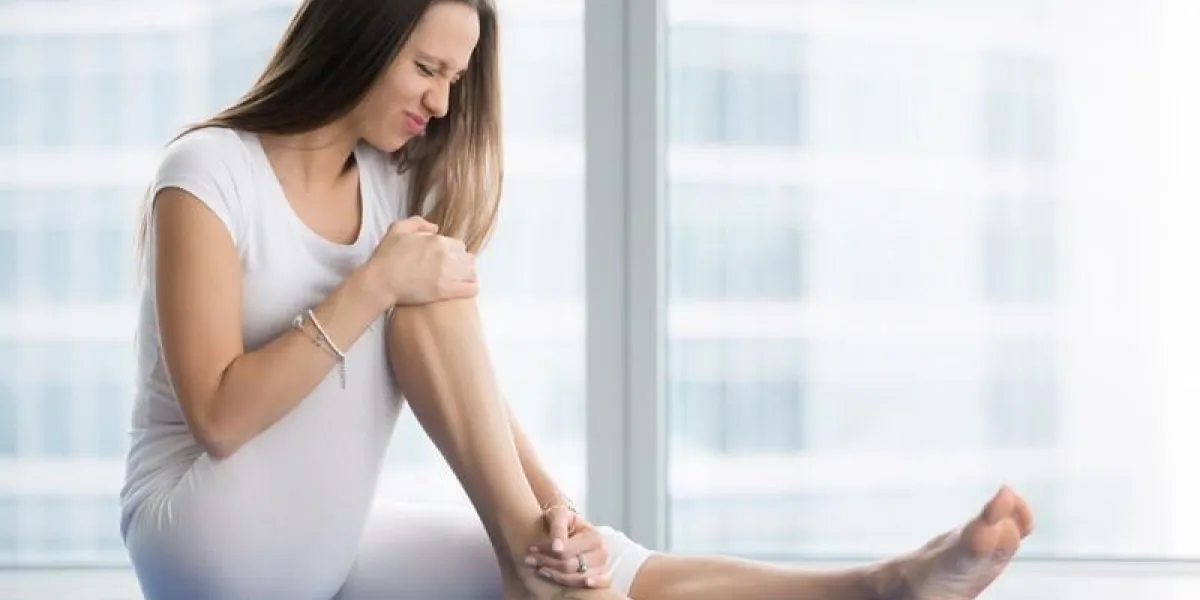 unhappy young woman sitting on the mat, grabbing an ankle, unable to start yoga work out because of sport injury, feeling pain beginner doing wrong exercise without coacher