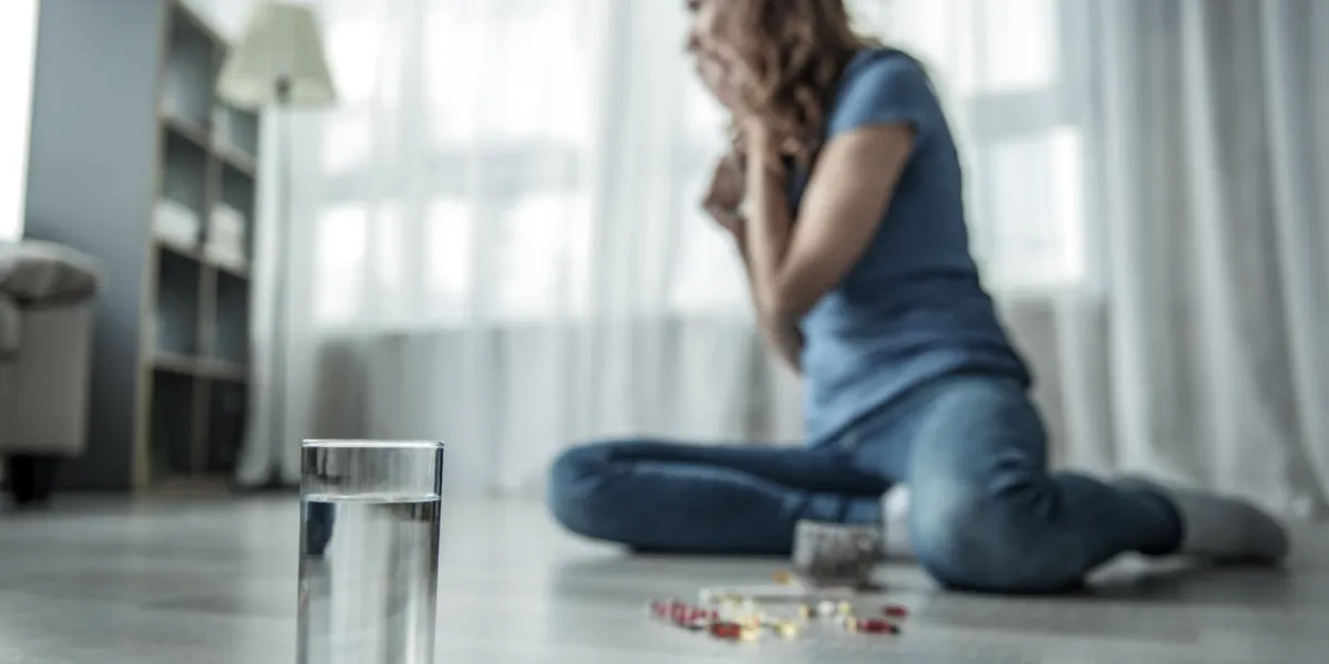 she is sitting on floor and crying focus on glass of water and drugs she is sitting on floor and crying focus on glass of water and drugs