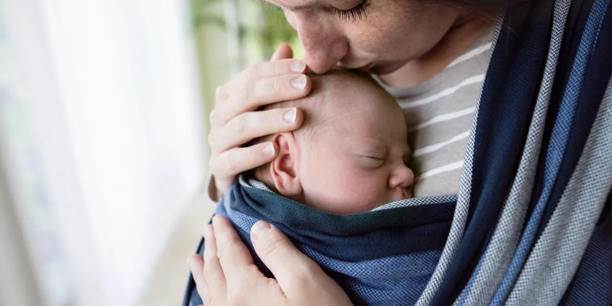 gros plan, belle jeune mère embrassant son fils nouveau-né en écharpe à la maison