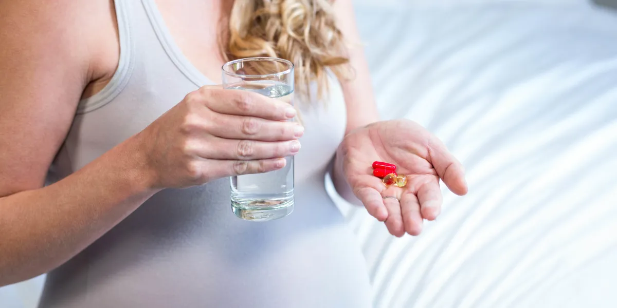 pregnant woman taking a pill with water in her bedroom