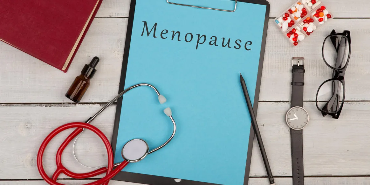 medecine concept - clipboard with text menopause, stethoscope, pills, book, watch and eyeglasses on white wooden background