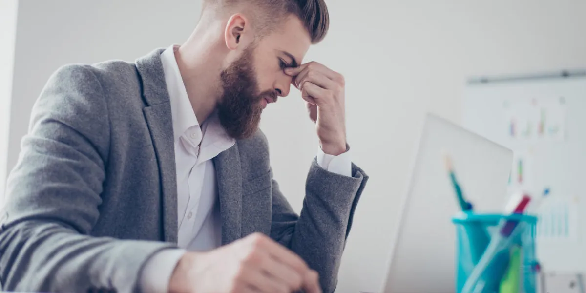 close up portrait of tired sick handsome young man with strong migraine grimace he is wearing the formalwear, sitting at the workplace