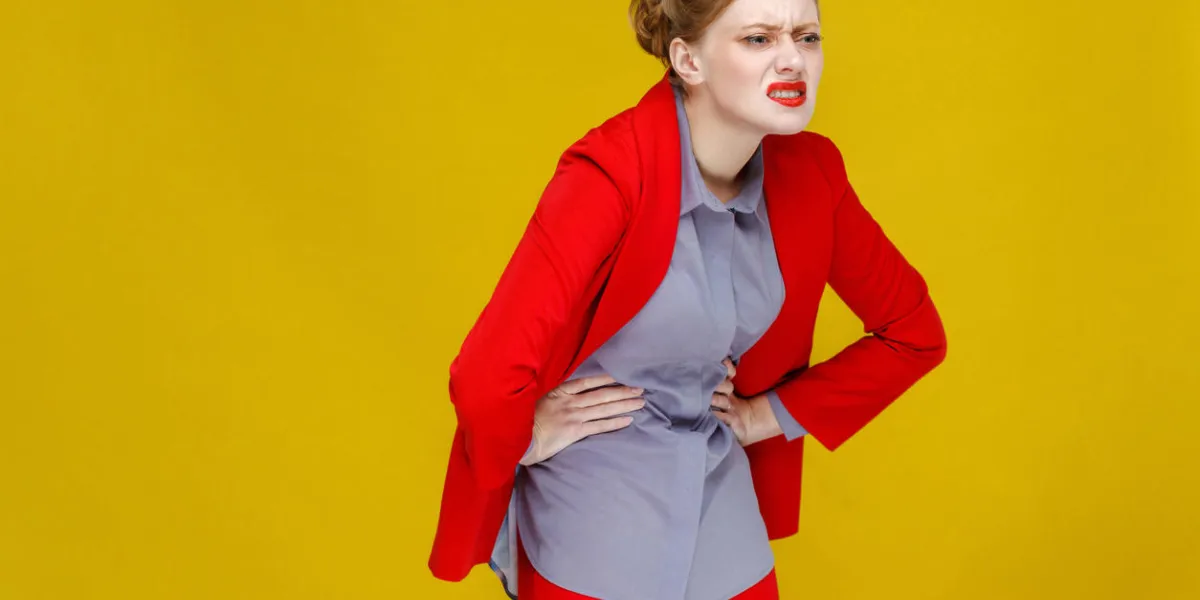 pms redhead business woman in red suit have period stomach pain studio shot, isolated on yellow background