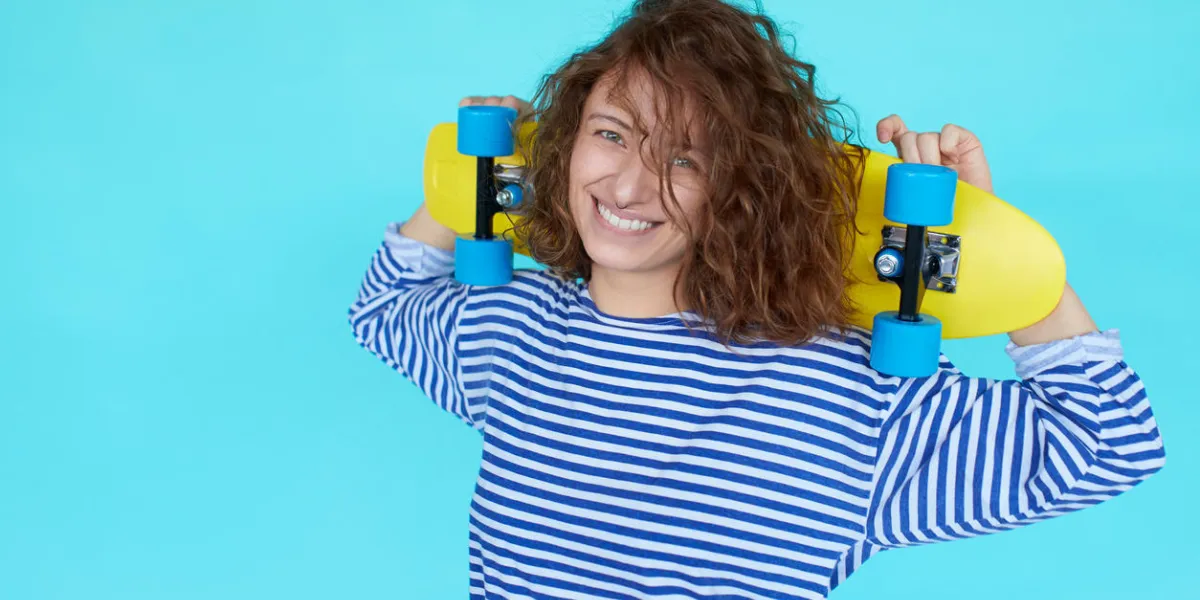 mode cool fille hipster avec des boucles et des vêtements colorés avec skateboard s'amuser contre le mur bleu mode cool fille hipster avec des boucles et des vêtements colorés avec skateboard s'amuser contre le mur bleu