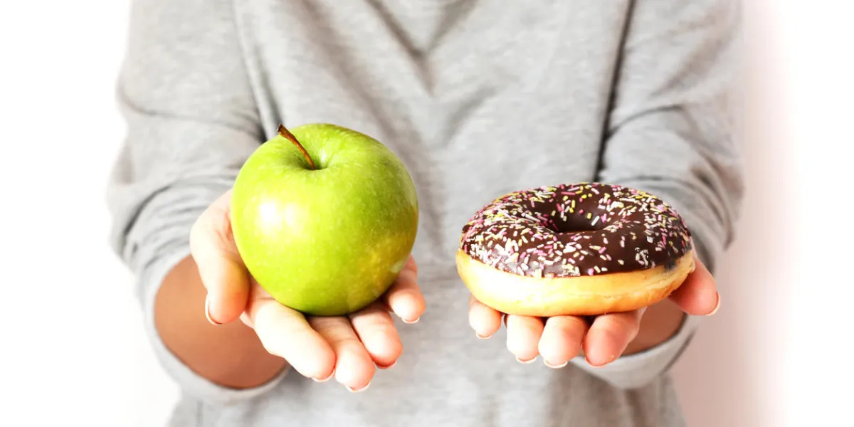 dieting concept with young woman choosing between healthy fruits and sweets, holding green apple and tasty chocolate donut
