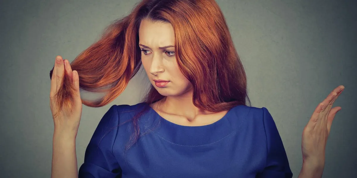 closeup malheureux bouleversé frustré jeune femme surpris elle perd des cheveux, a remarqué des pointes fourchues dégarni hairline fond gris visage humain expression émotion beauté coiffure concept