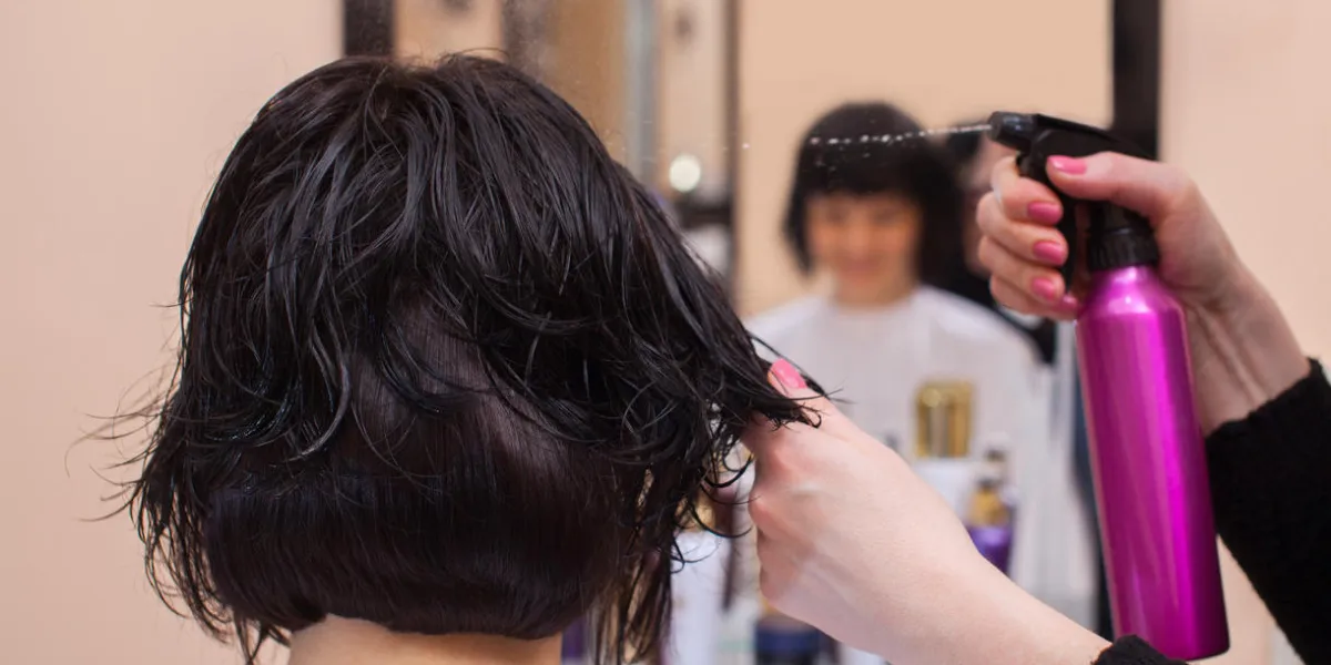 le coiffeur avant de sécher ses cheveux saupoudre un spray sur les cheveux de la brune dans le salon de beauté le coiffeur avant de sécher ses cheveux saupoudre un spray sur les cheveux de la brune dans le salon de beauté