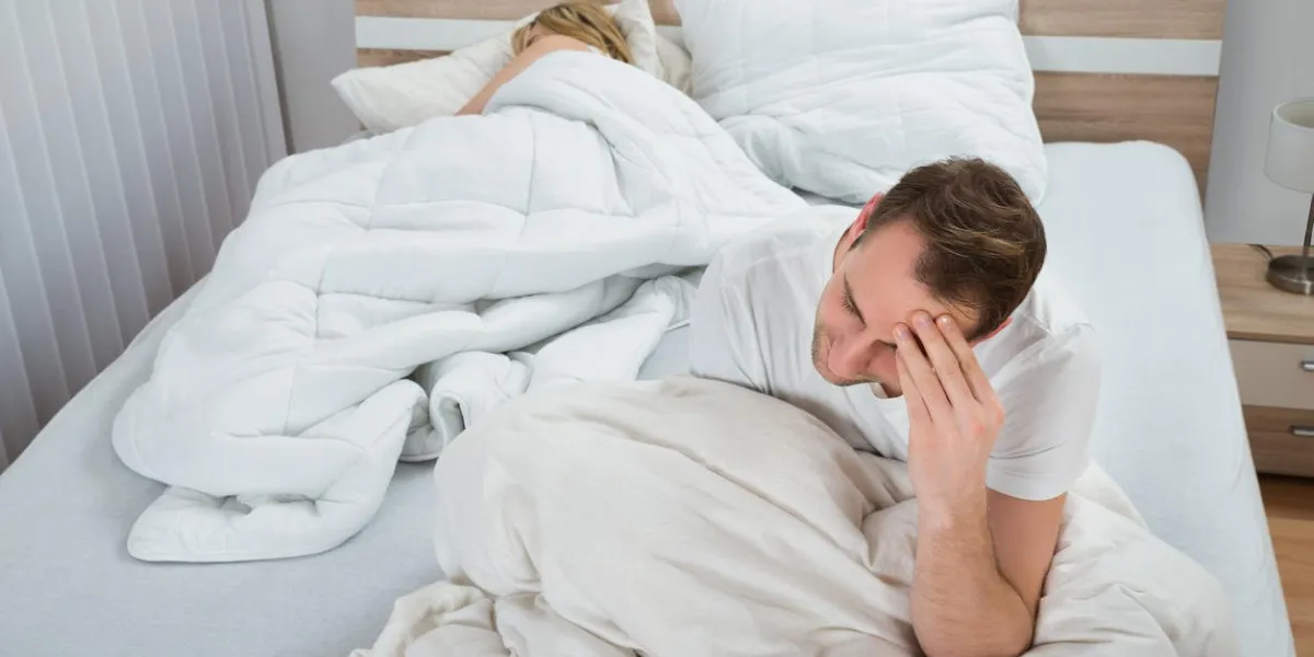 depressed man sitting on bed while woman sleeping in bedroom