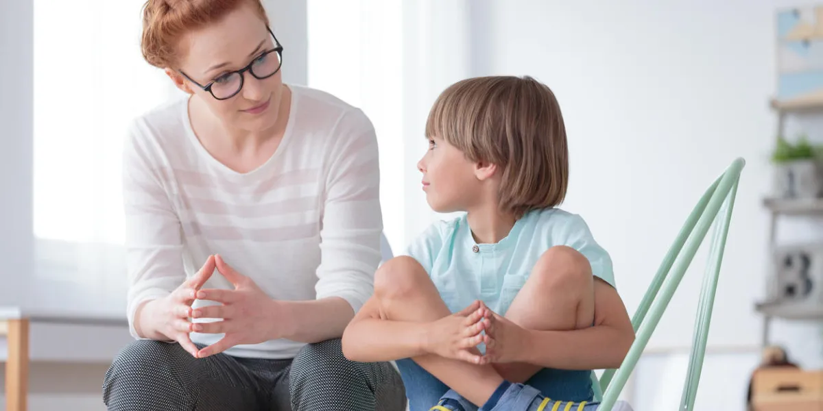young female school psychologist having serious conversation with smart little boy at office young female school psychologist having serious conversation with smart little boy at office