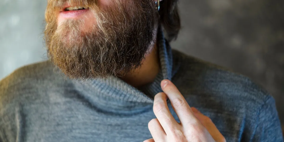 bearded man in a gray sweater turtleneck pulling his collar with his fingers discomfort hot sweat concept bearded man in a gray sweater turtleneck pulling his collar with his fingers discomfort hot sweat concept