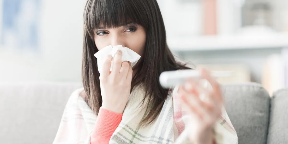 young sick woman with cold and flu, she is blowing her nose and measuring her body temperature